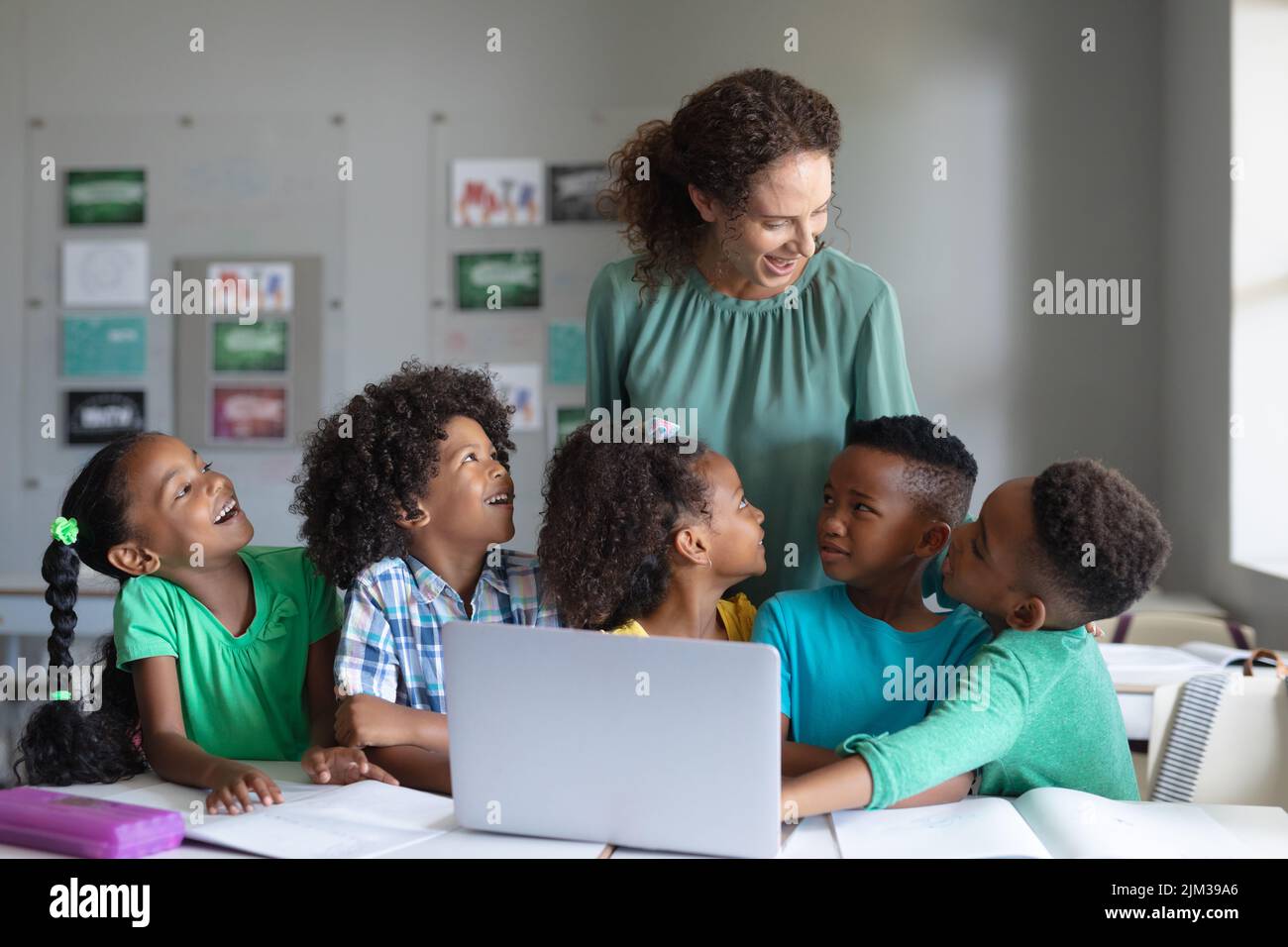 Smiling caucasian young female teacher teaching laptop to african american elementary students. unaltered, education, childhood, teaching, learning, w Stock Photo