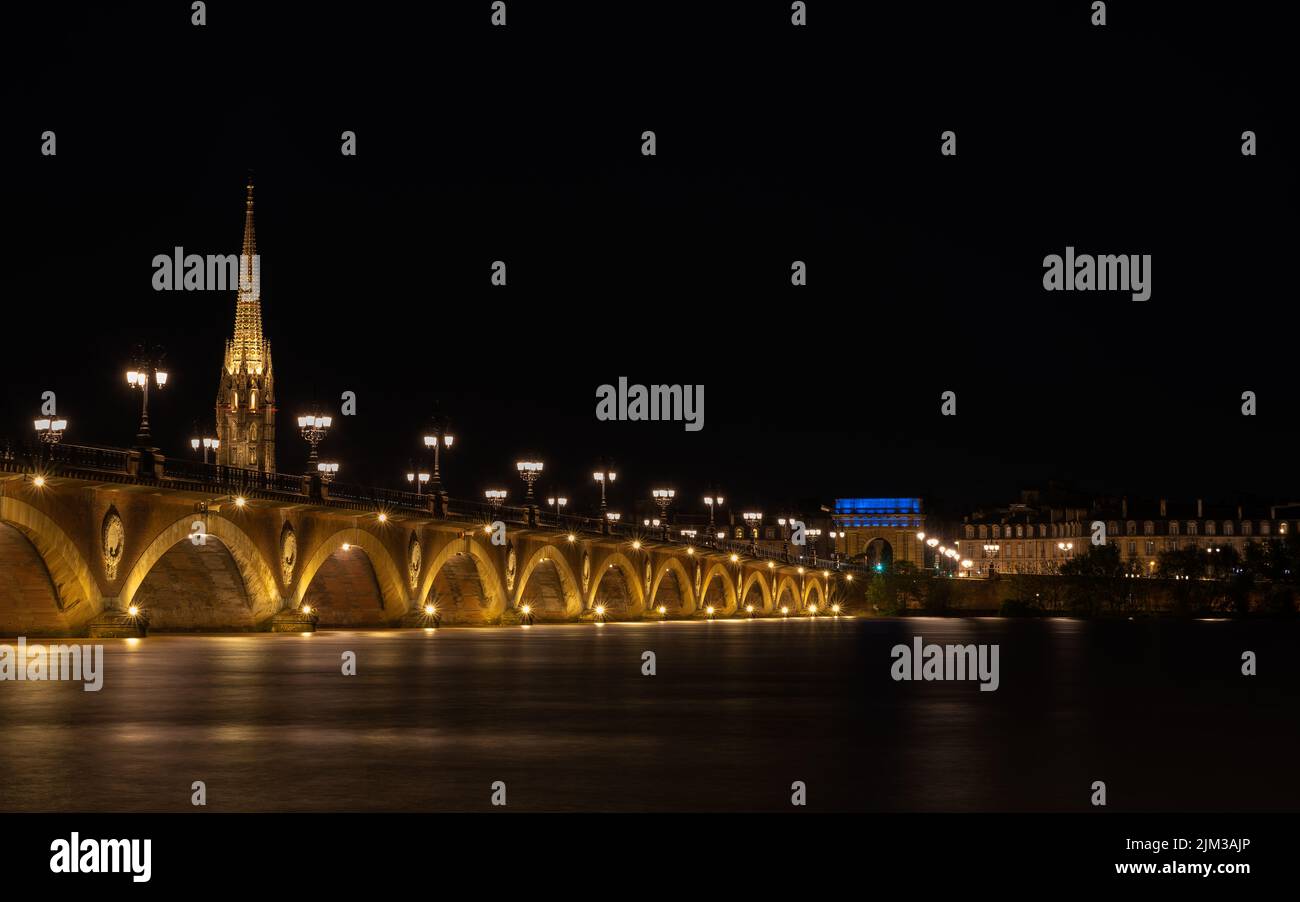 Pont de Pierre spanning the River Garonne in the city of Bordeaux illuminated at night with the Basilique Saint-Michel in the background Stock Photo