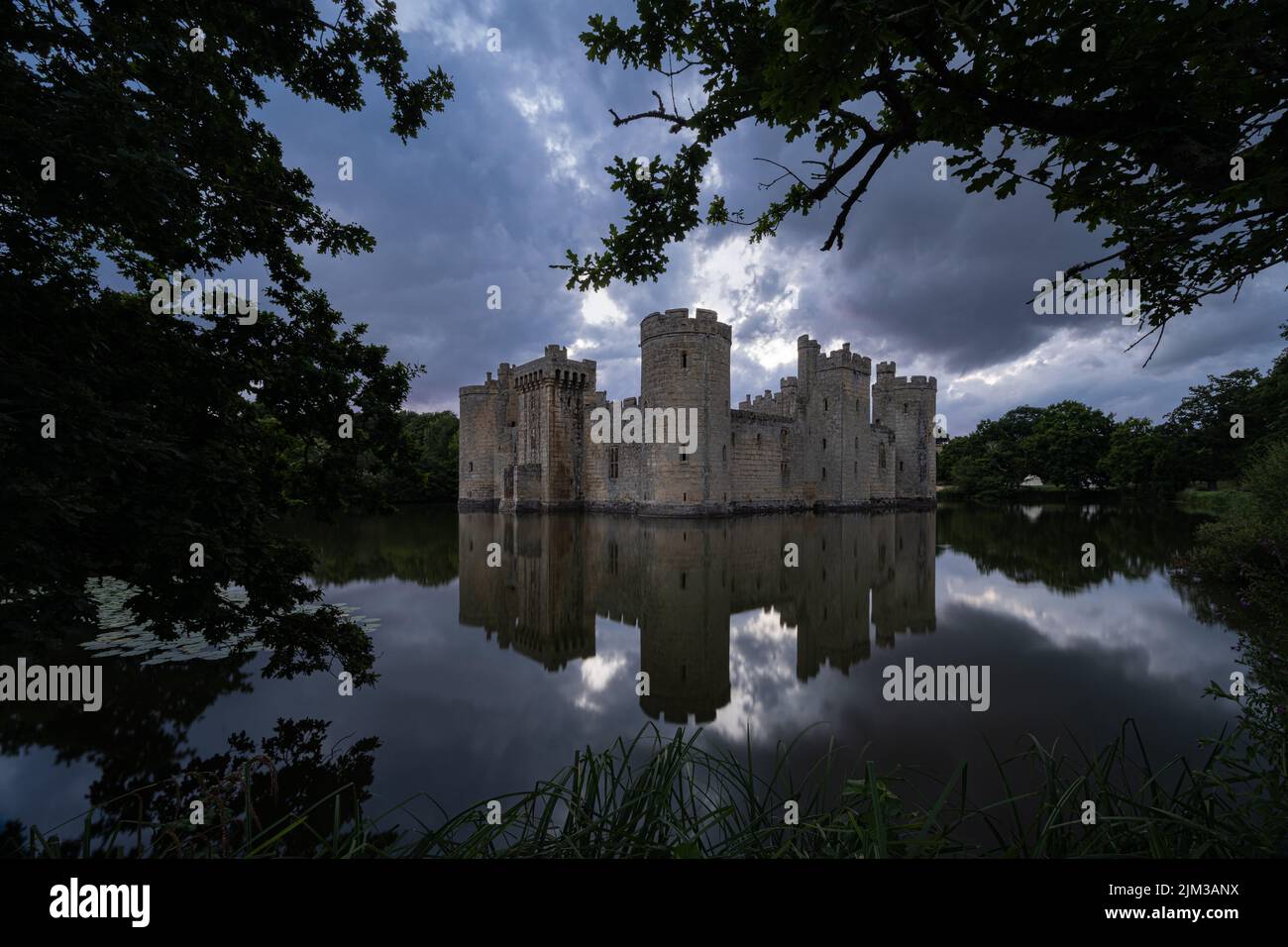 Bodiam Castle in East Sussex at sunset with the castle reflected in the surrounding moat and framed by trees Stock Photo