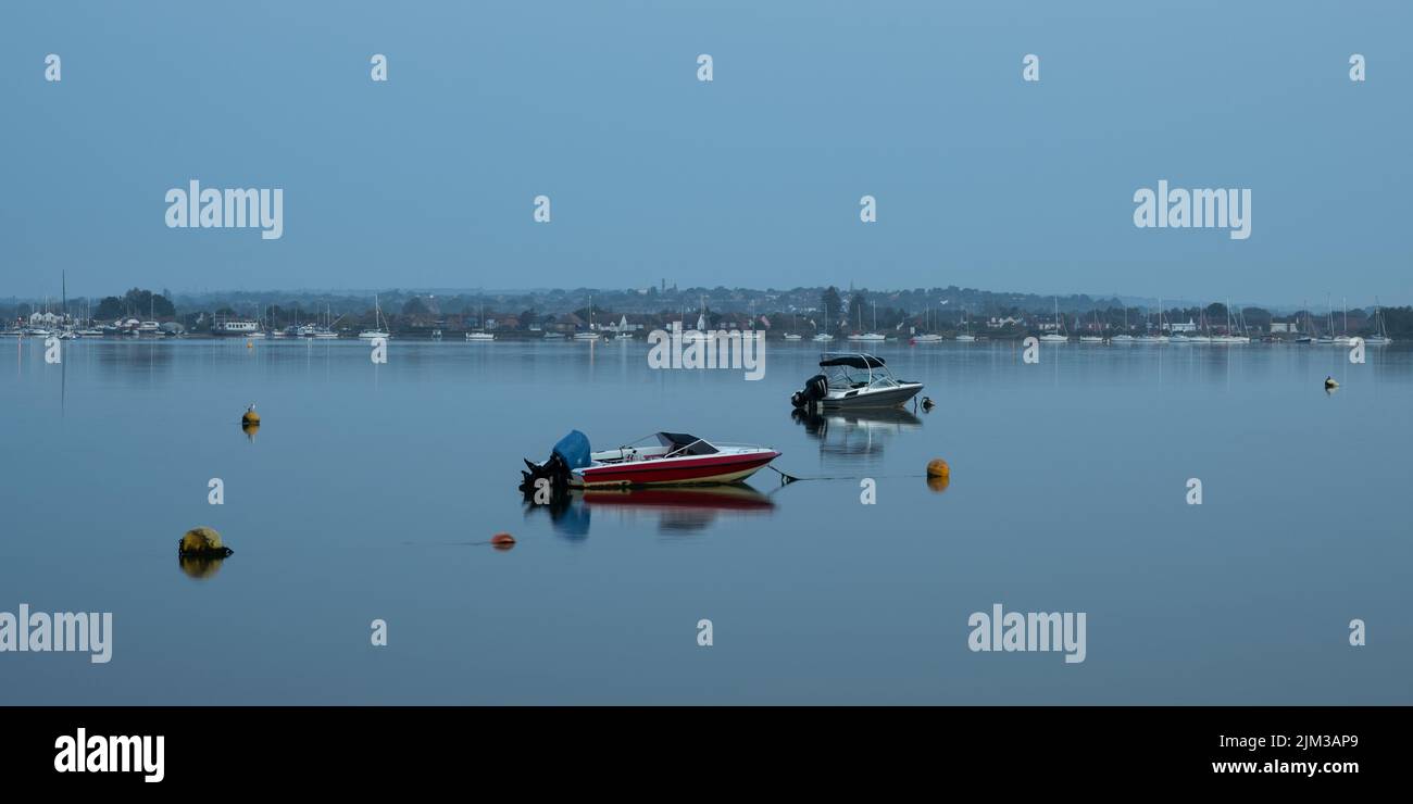 Speed boats moored on the river Blackwater at Heybridge Basin, Essex  shortly after sunrise with the boats reflected in the water Stock Photo
