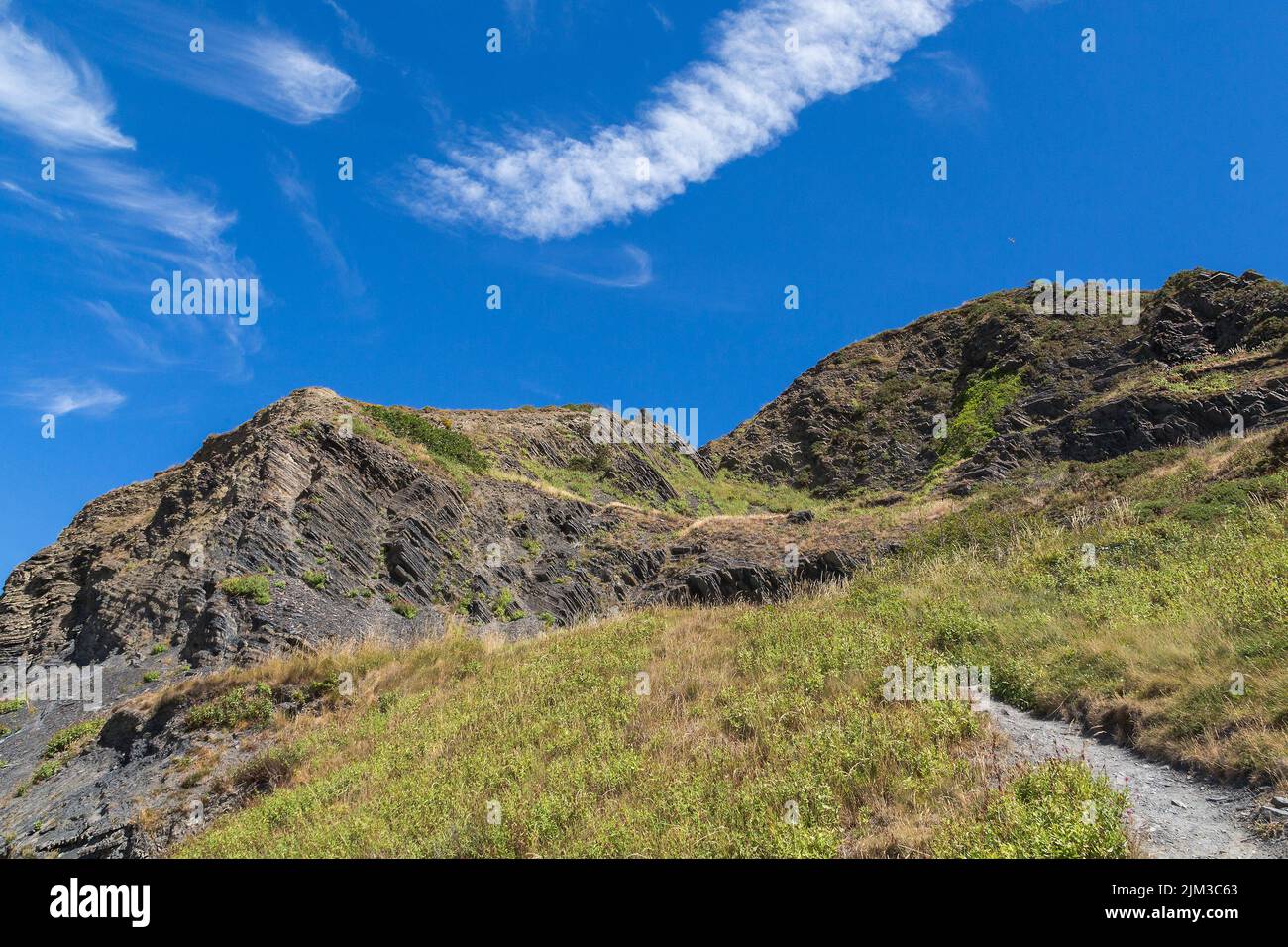 Scenic landscape of a steep hill trail featuring rocks set against a blue sky. Health, fitness, walking, hiking or active leisure time concept. Stock Photo