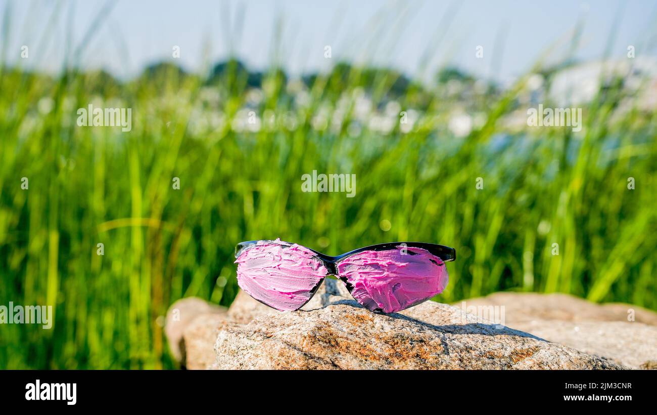 Pink covered sunglasses on rock with green grass on background and copy space Stock Photo