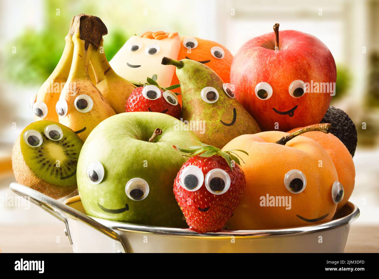 Detail of a fruit bowl full of fruit with eyes and a mouth on the bench in a bright kitchen. Fruits and vegetables child healthy eating concept. Stock Photo