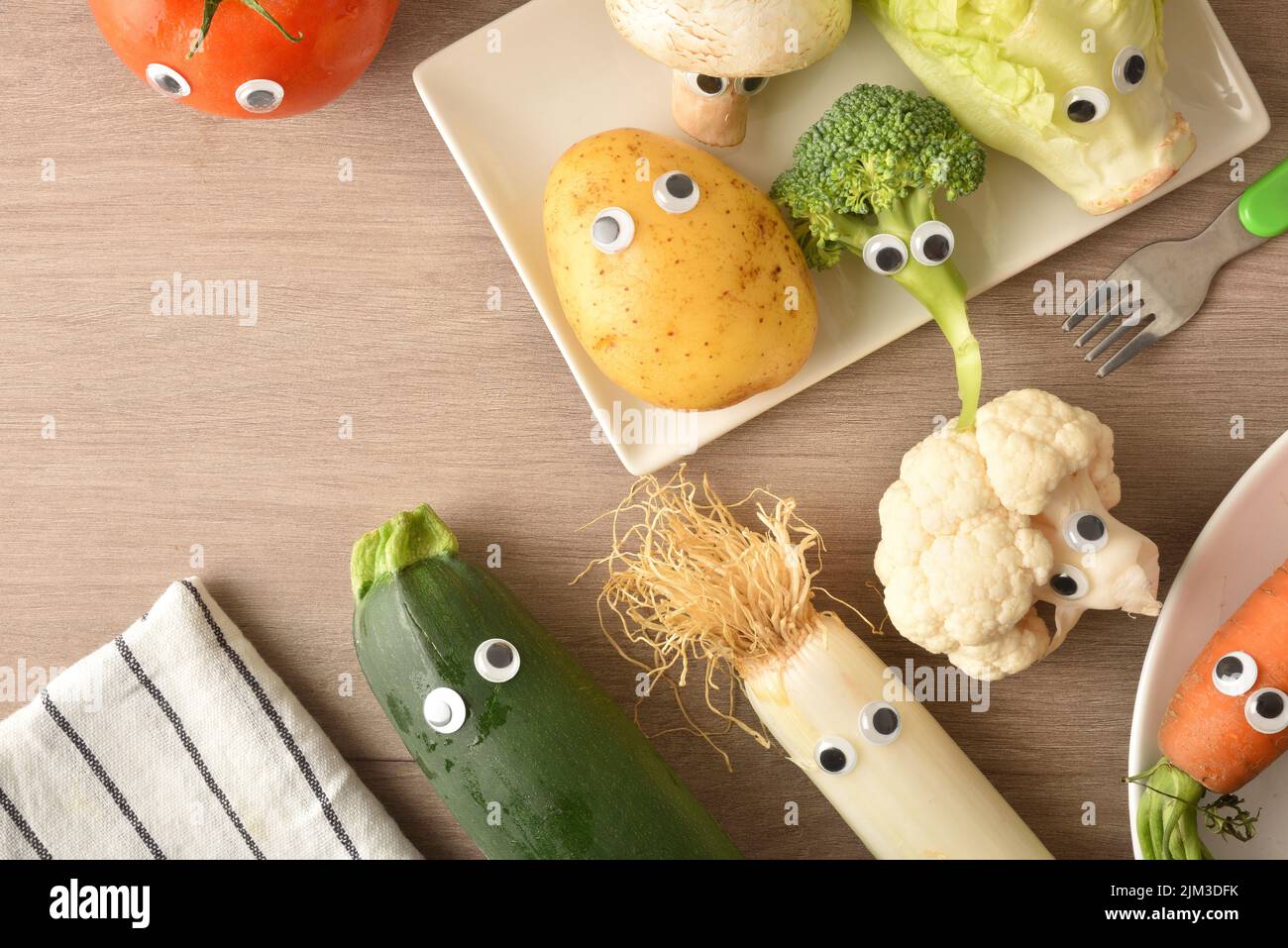Child nutrition concept with detail of raw vegetables with eyes on wooden table. Top view. Stock Photo