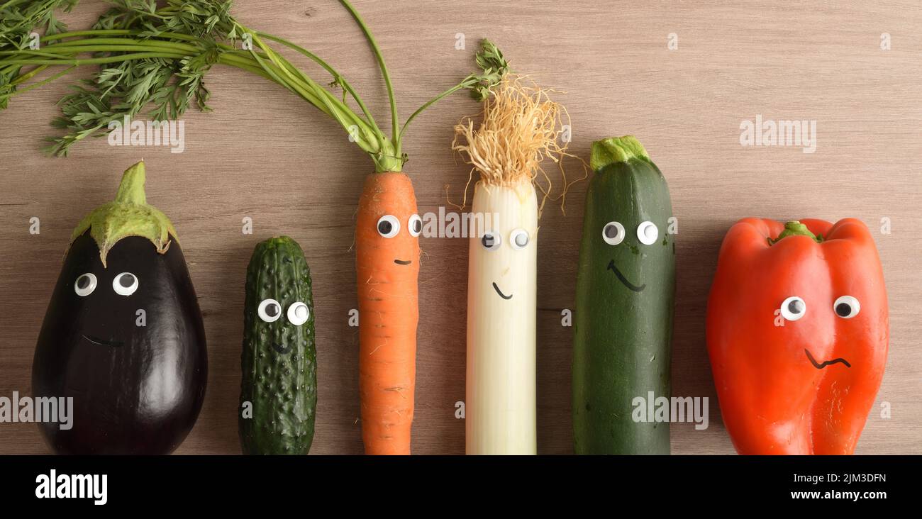 Row of funny vegetables with eyes and mouths as a concept for motivating children to eat. Top view. Stock Photo