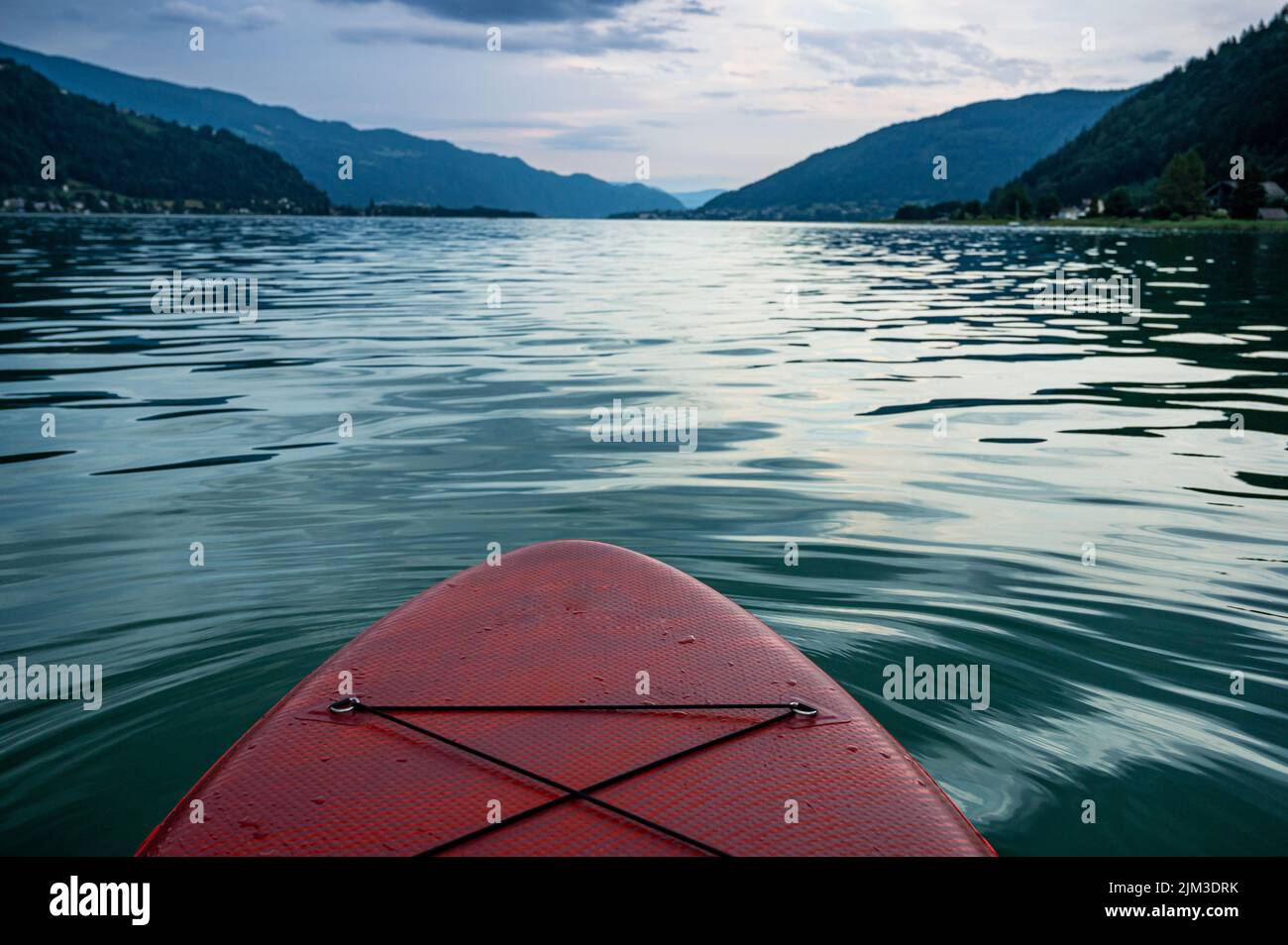 red SUP board on lake Ossiach in Austria with view of mountains in the evening just before a thunderstorm Stock Photo
