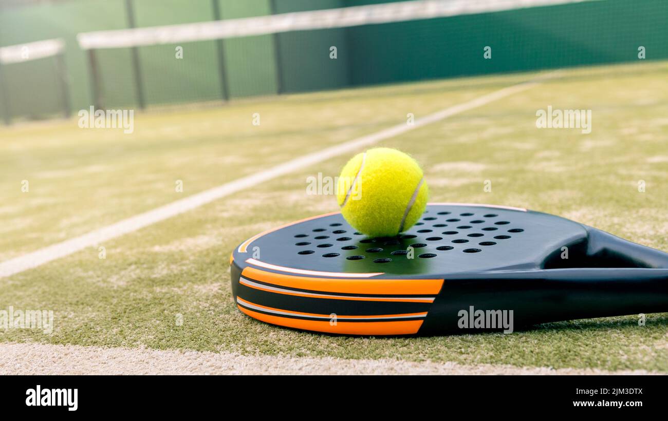 Yellow ball over padel tennis racket in green court outdoors with natural lighting. Paddle is a racquet game. Professional sport concept with copy spa Stock Photo