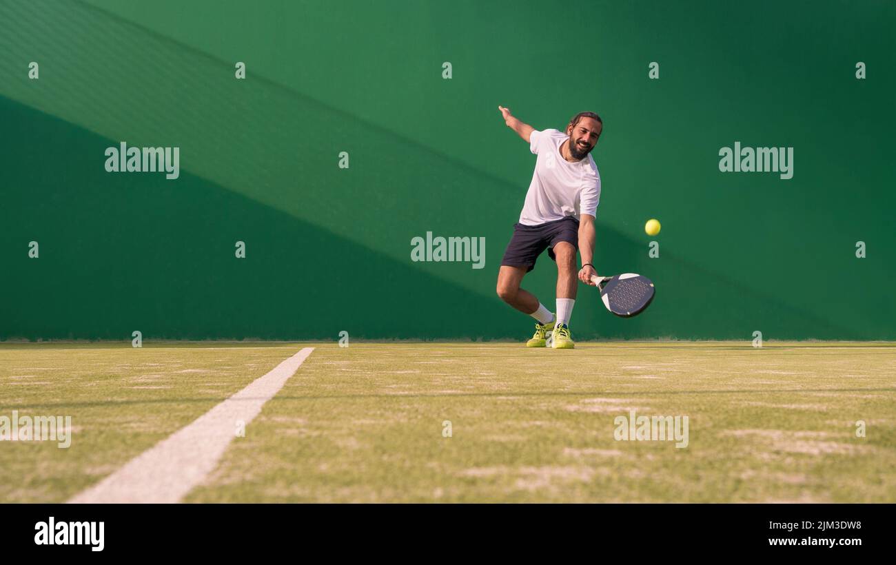 Professional monitor of padel jump to the ball with a black racket. Class to student on outdoor tennis court. Man paddel player playing a match in the Stock Photo