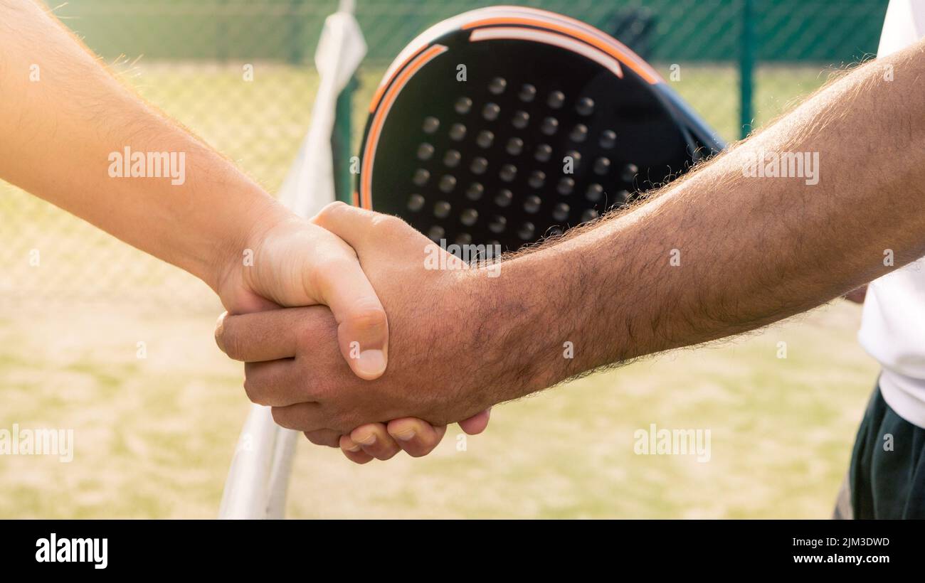 Male padel players handshake after win a padel match in a green paddel court outdoor. Tennis players shake hands Stock Photo