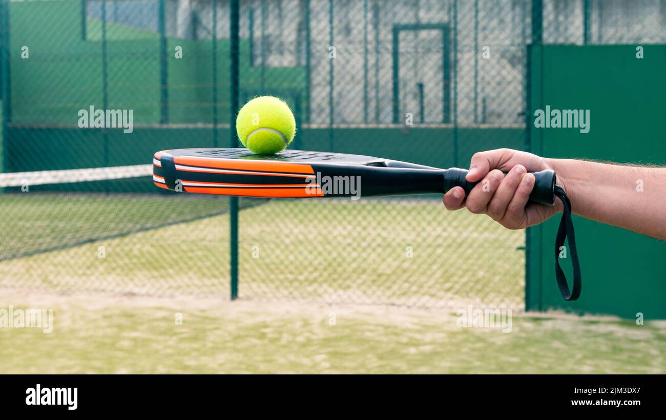 One caucasian man with the ball on top of the padel racket at a green court grass turf outdoors. Paddle is a racquet game. Professional sport concept Stock Photo