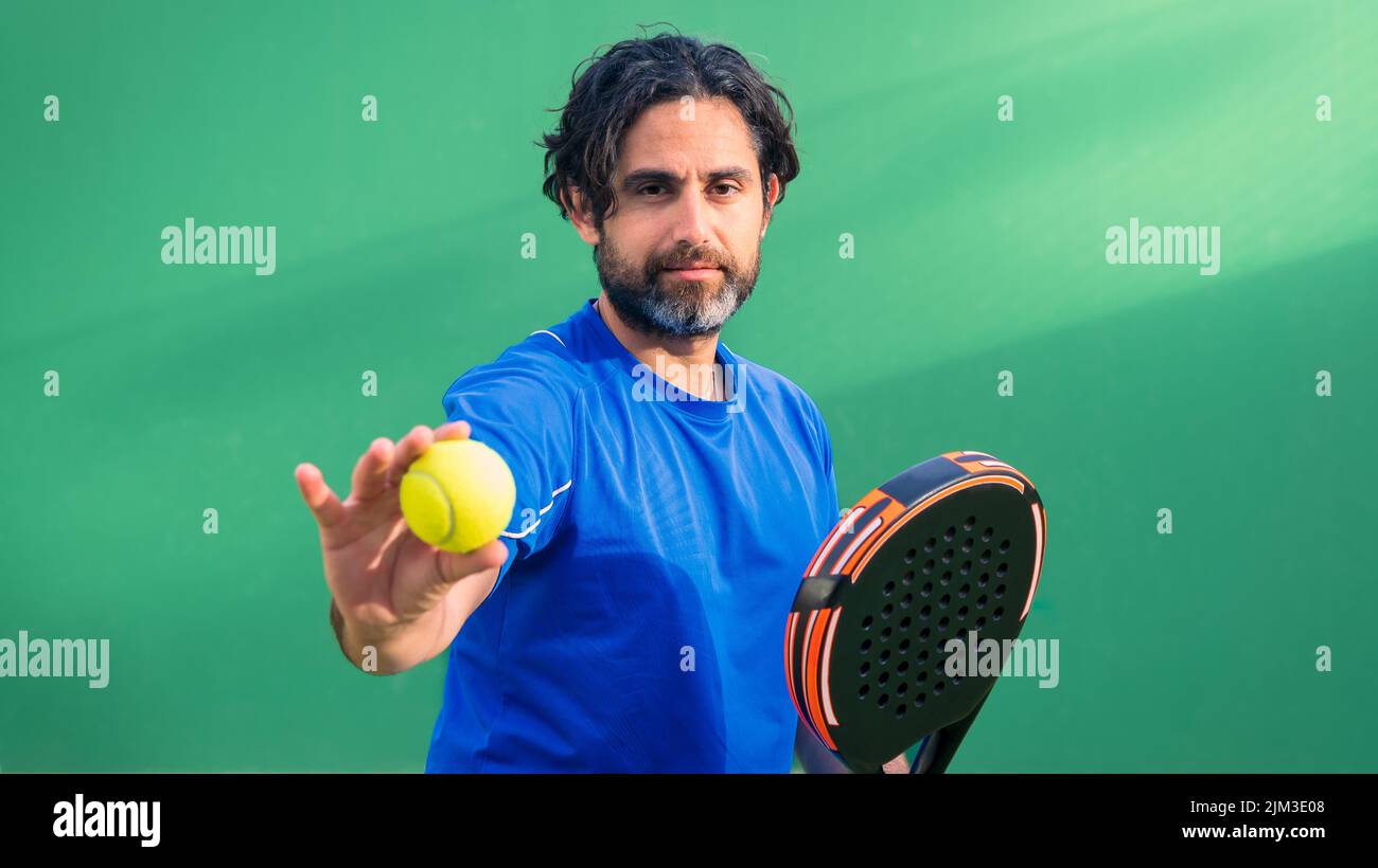 Monitor of padel holding black racket with yellow tennis ball in the hand. Class to student on outdoor tennis court. Man paddel player playing a match Stock Photo