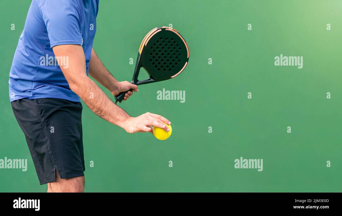 One caucasian man playing a match in the open with black padel racket and yellow ball at court outdoors. Paddle is a racquet game. Professional sport Stock Photo