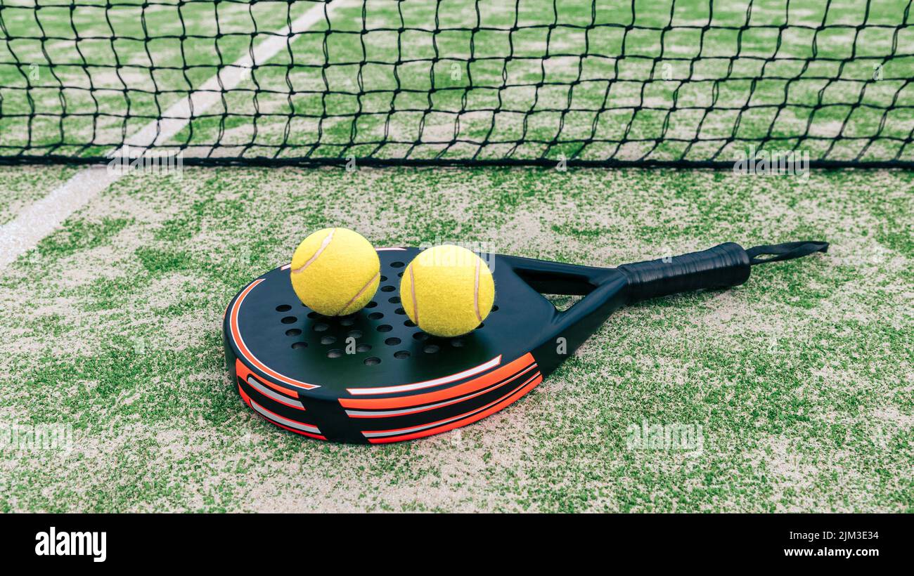 Yellow balls over padel tennis racket behind net in green court outdoors with natural lighting. Paddle is a racquet game. Professional sport concept w Stock Photo