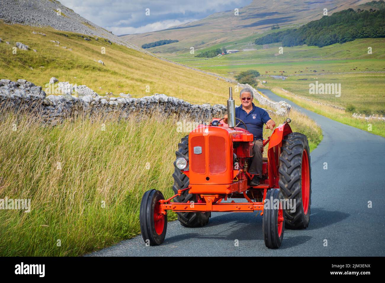 31.07.2022 Ingleton, North Yorkshire, UK A man wearing sunglasses, a blue shirt driving a vintage red tractor in the Yorkshire Dales Stock Photo