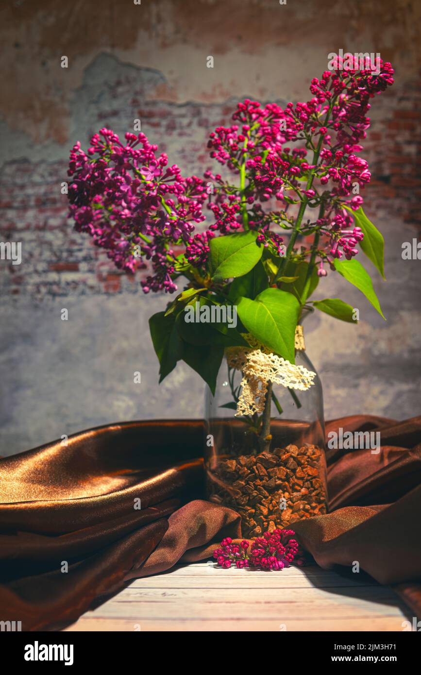 A vertical shot of lilac in a vase with silk clothing resembling a ...