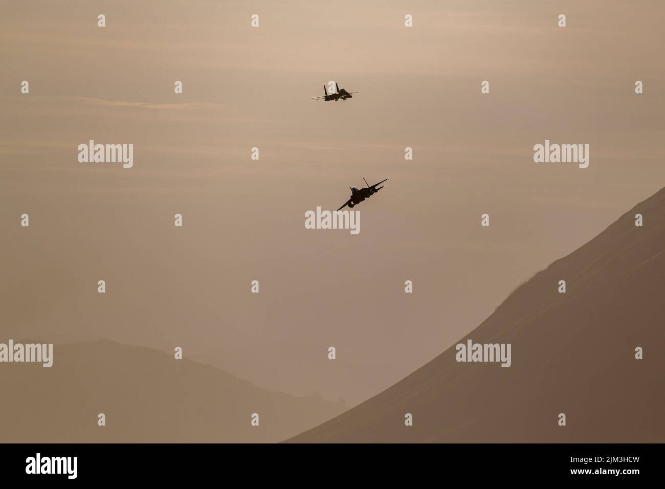 A low angle shot of military airplanes flying against mountains in monochrome colors Stock Photo