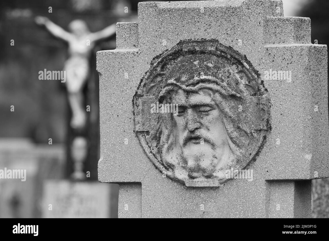 A selective focus of the carved face of Jesus Christ on the blurred background of crucified Christ on the cross in Pecs cemetery, Hungary Stock Photo
