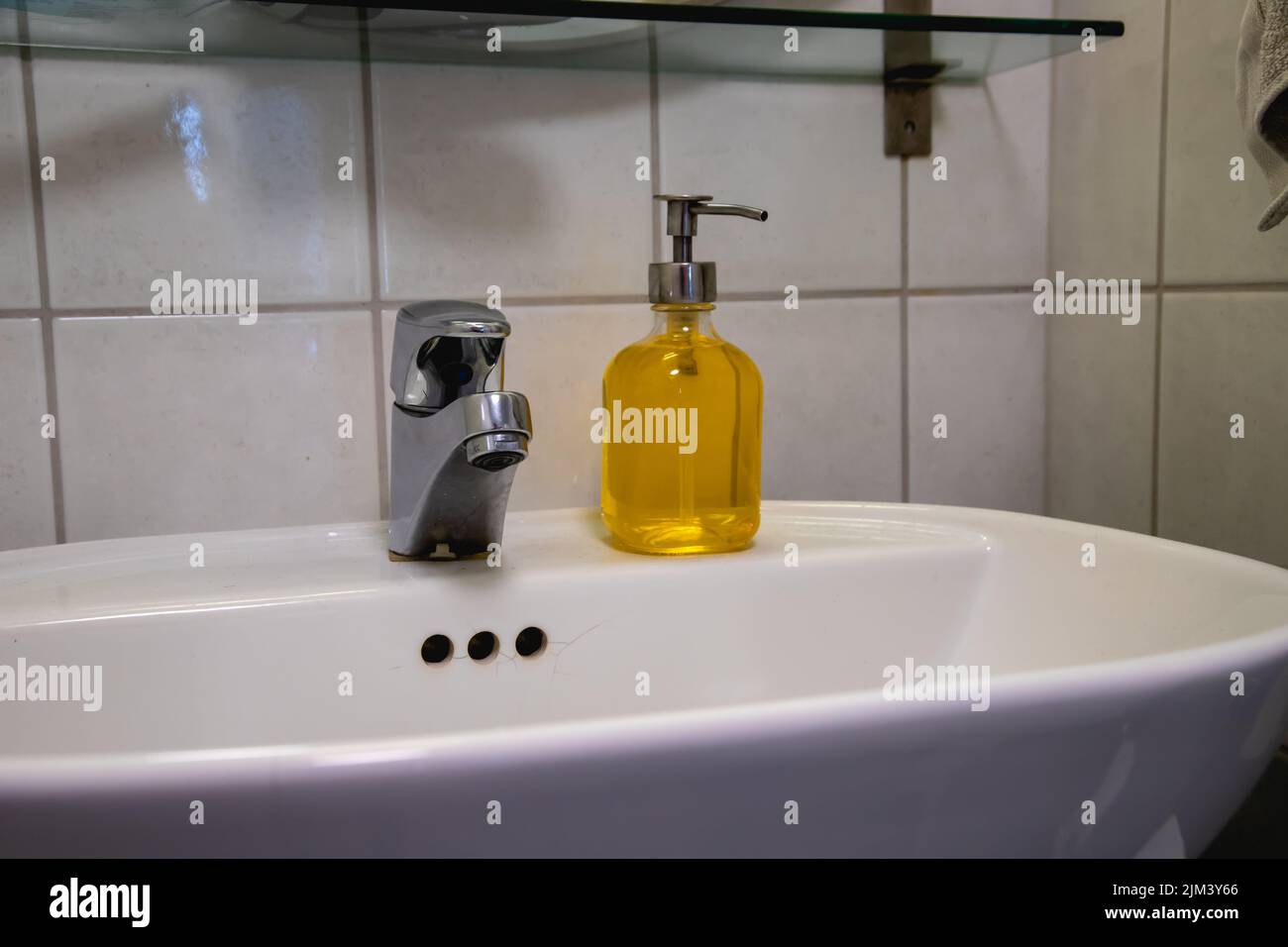 A yellow liquid hand soap on the sink in the bathroom with white wall