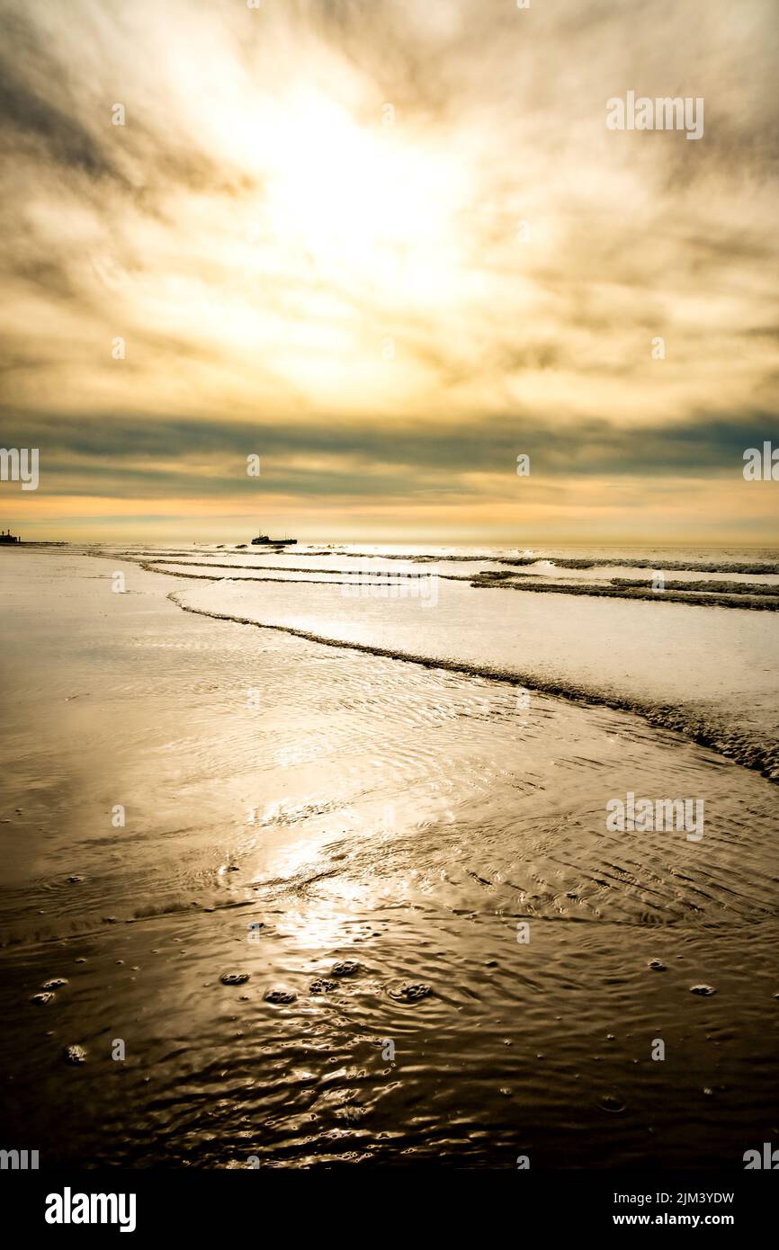 Amazing colorful sunset on a sandy beach at the sea under a sky painted with clouds and a golden sun. Picturesque nature scenery.Clouds reflected in water. Zen-like tranquil atmosphere no people. Travel inspiration concept space for text. High quality photo Stock Photo