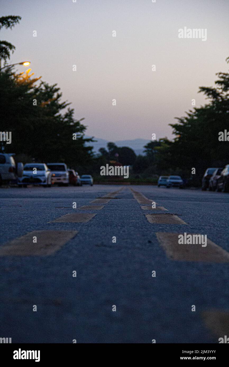 A vertical shot of an asphalt road with parked cars at the parking lots ...