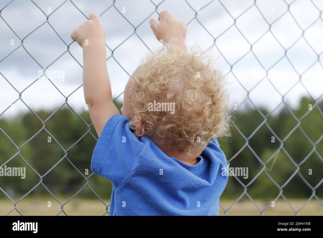 A backshot of a baby boy 3 years old standing behind a grid fence in ...