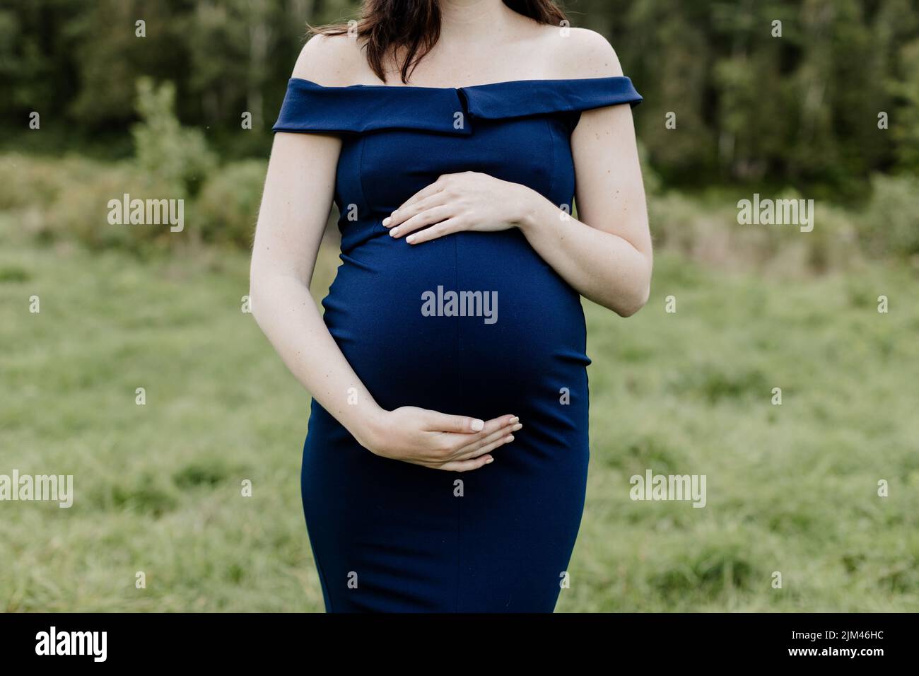 A young 38 weeks pregnant woman in a blue dress holding her belly Stock Photo