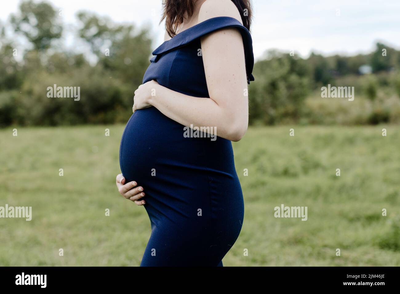 A young 38 weeks pregnant woman in a blue dress holding her belly Stock Photo