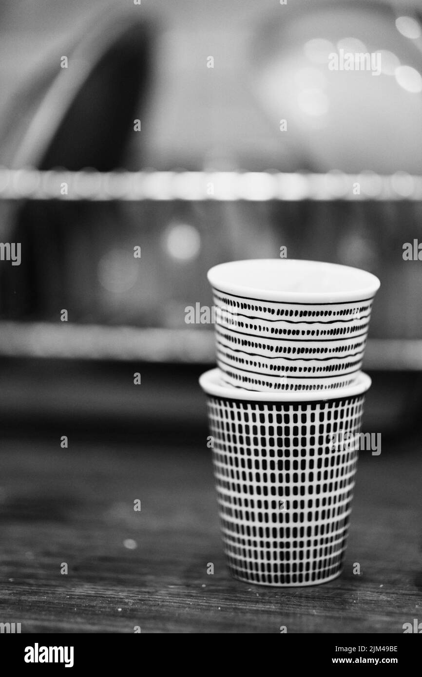 A vertical grayscale closeup shot of two patterned eco-friendly cups one in another on wooden surface Stock Photo