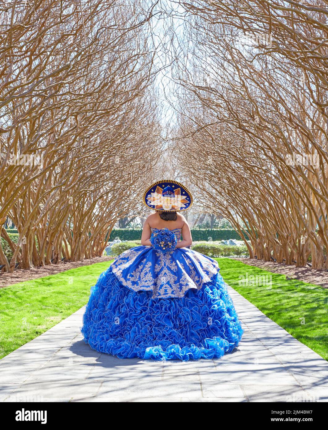 A vertical shot of a female posing in a forest in a blue Quinceanera Dress Stock Photo