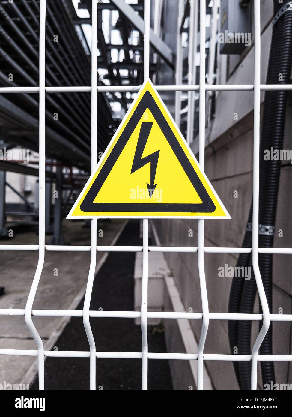 Danger Sign High voltage in the yellow triangle on the metal fence of the grid Stock Photo