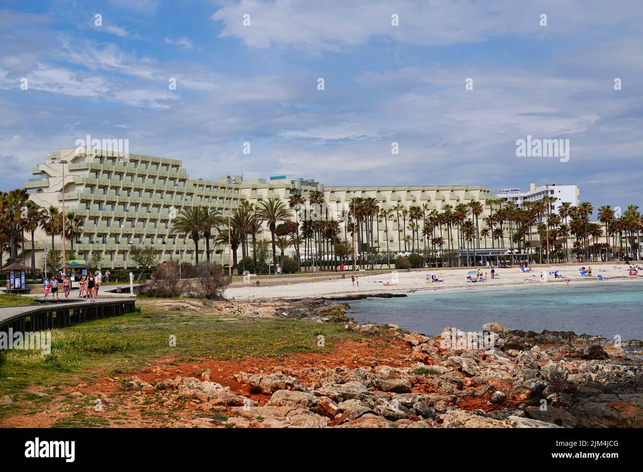 Picture shows a selective iew of the sandy beach of Sa Coma, Mallorca, with hotels, palm trees, lava rock and jetty Stock Photo