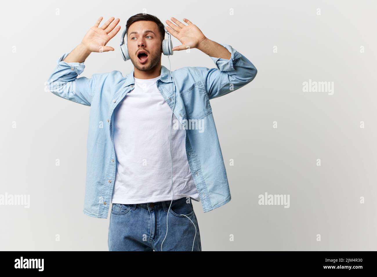 Excited shocked happy tanned handsome man in casual basic t-shirt headphones hold palms up listen cool music posing isolated on over white studio Stock Photo