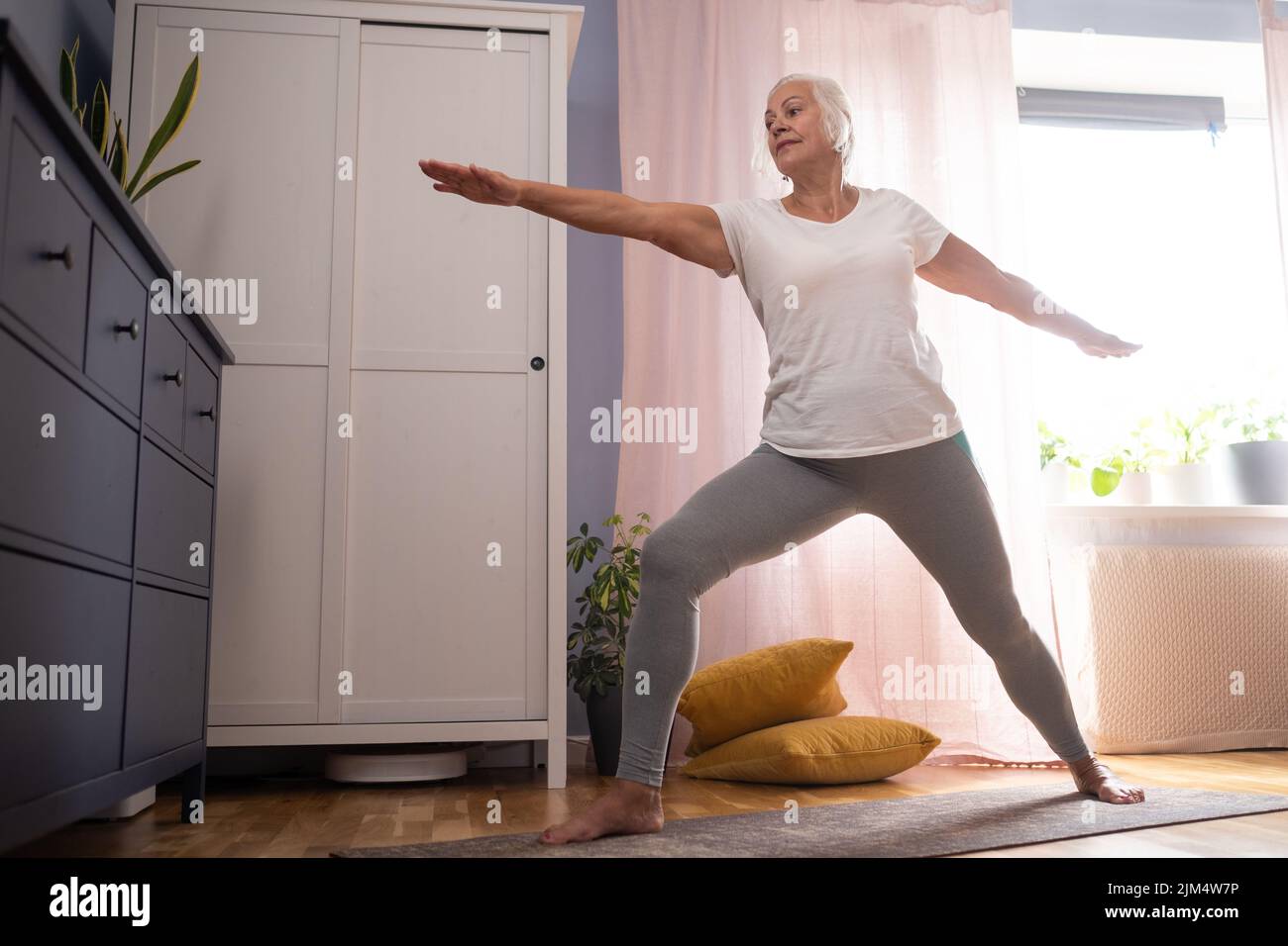 Happy senior lady doing yoga asana at living room. Stock Photo