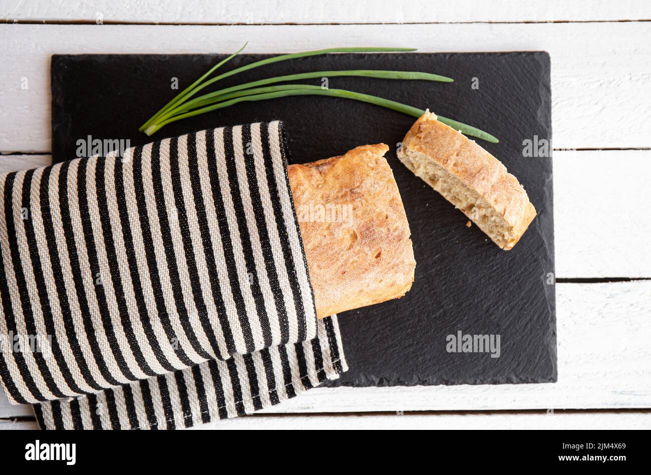 Flat lay view freshly baked homemade wheat flour loaf of bread on black stone serving board in home kitchen. Stock Photo