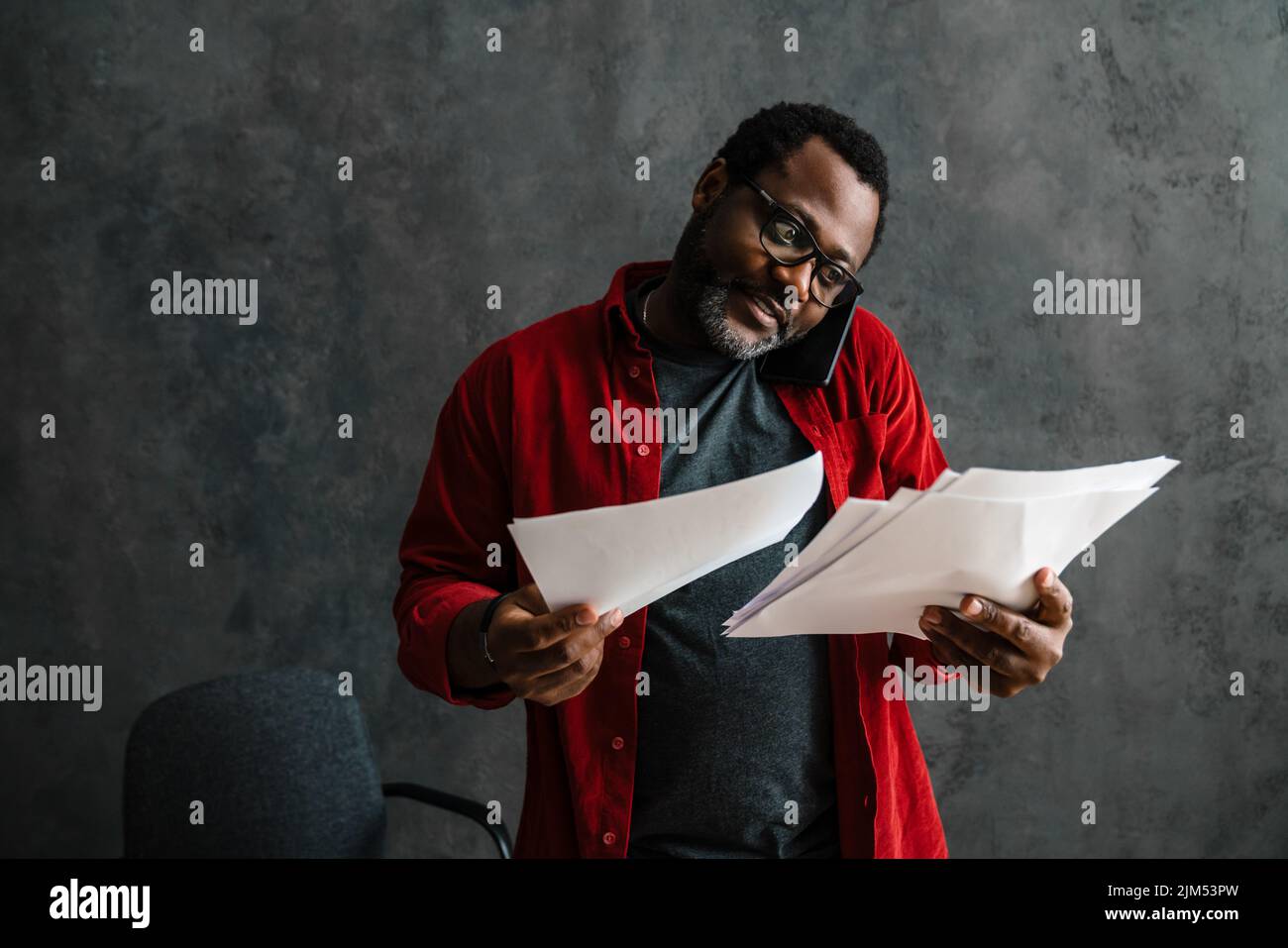 Black man talking on cellphone while working with papers indoors Stock Photo