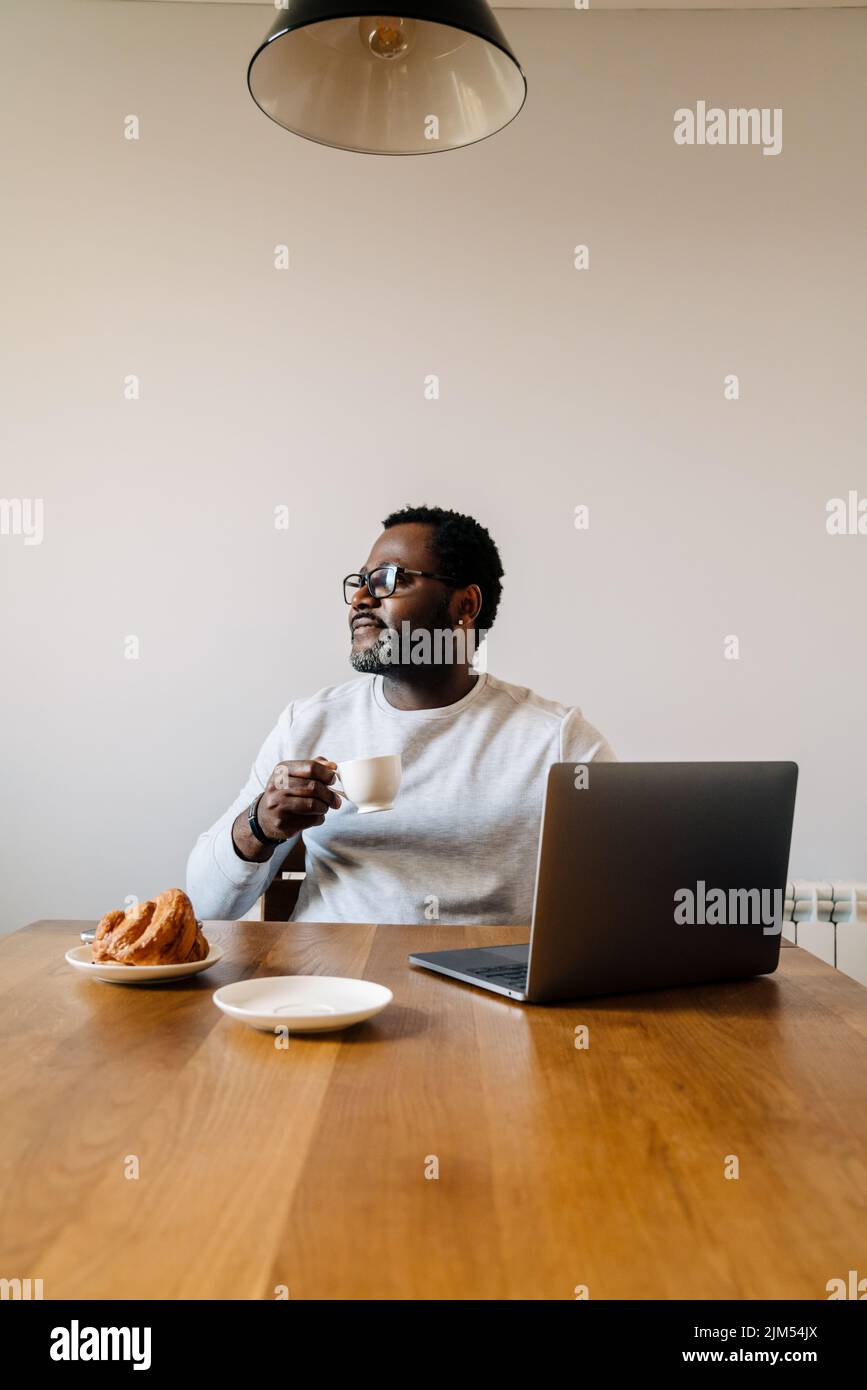Black man working with laptop while having breakfast at home Stock Photo