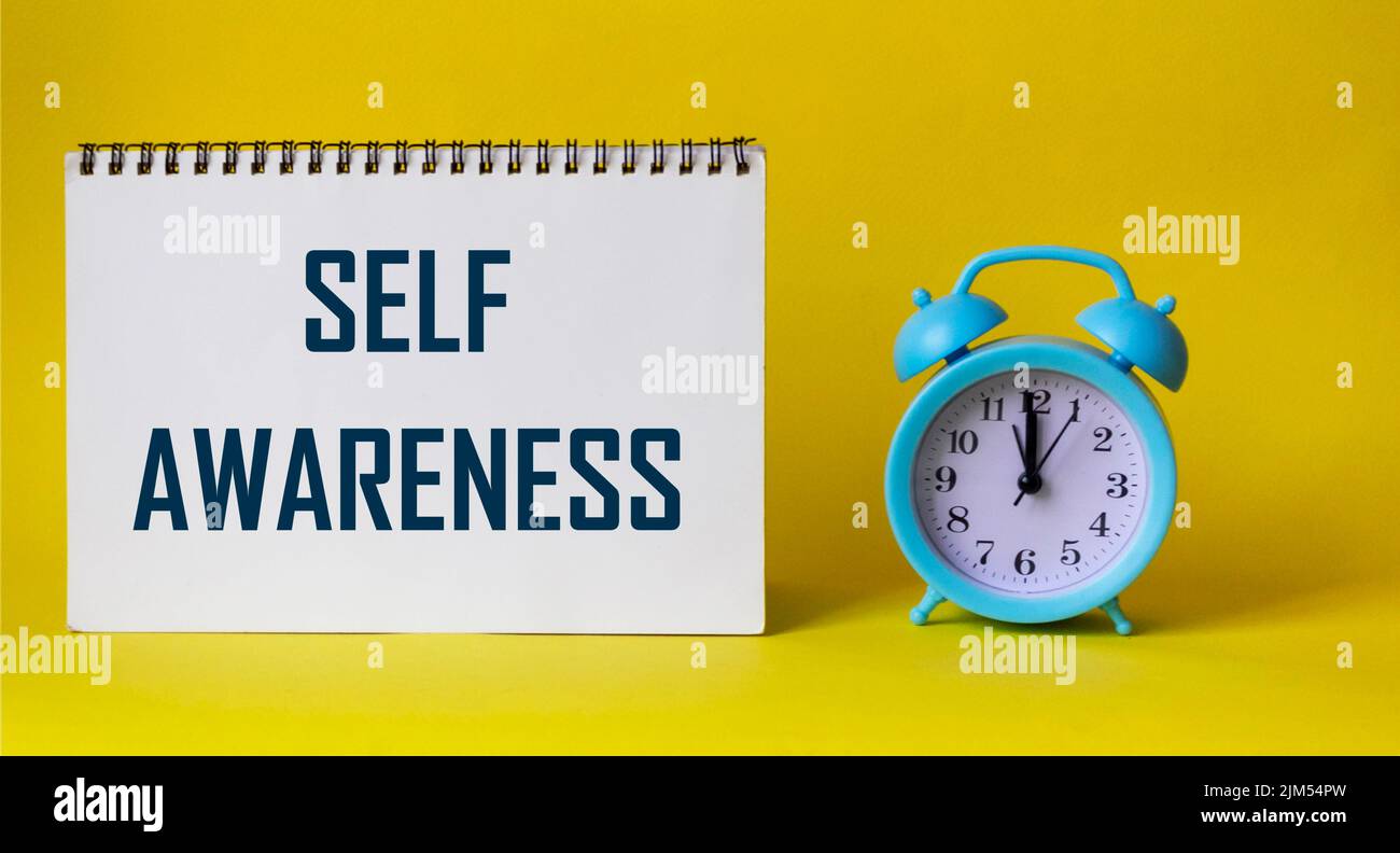 The word Self-awareness on a notepad and a yellow background, next to the clock Stock Photo