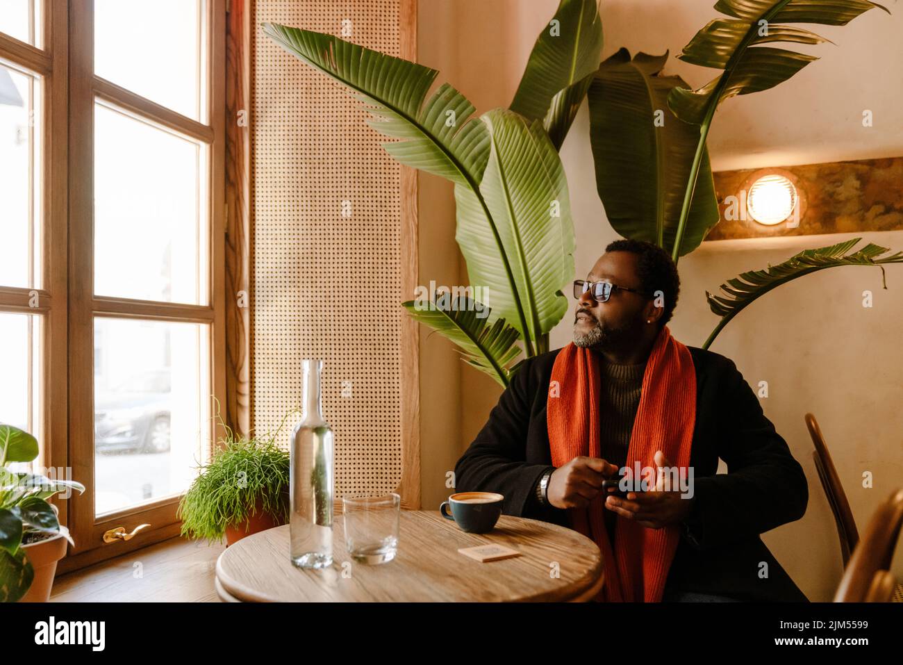 Black man using cellphone while drinking coffee in cafe indoors Stock Photo
