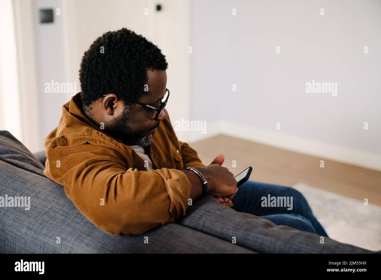 Black bearded man using cellphone while sitting on sofa at home Stock Photo