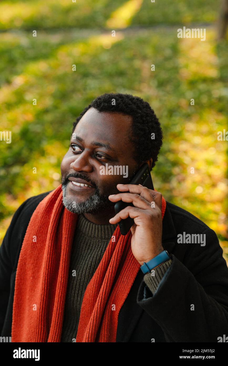 Black bearded man talking on cellphone while strolling at park Stock Photo