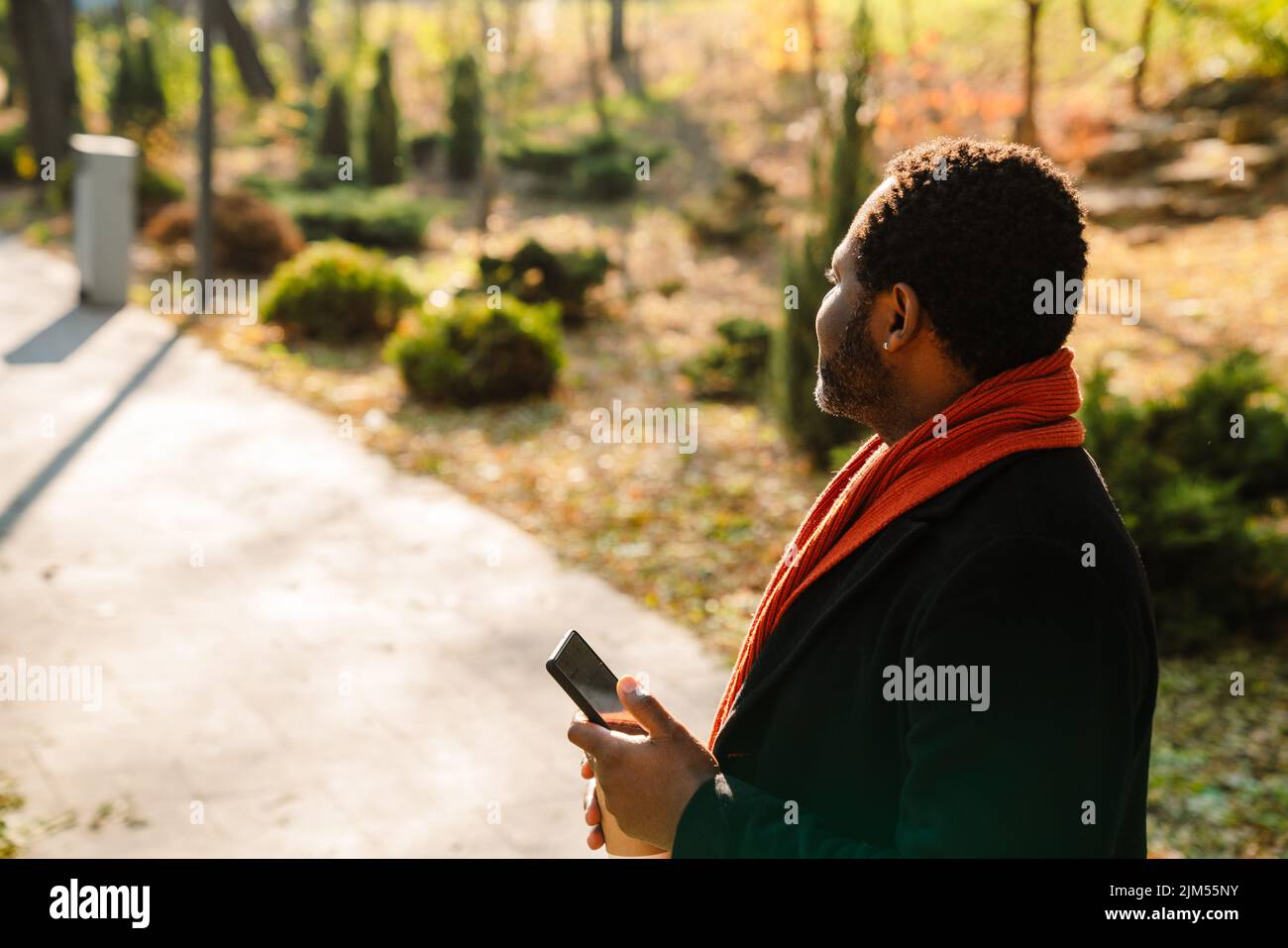 Black bearded man using cellphone while strolling in park Stock Photo