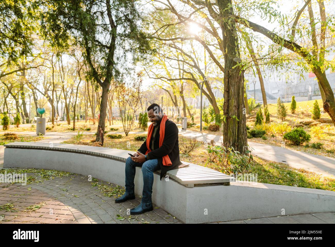 Black bearded man using cellphone while sitting on bench at park Stock Photo