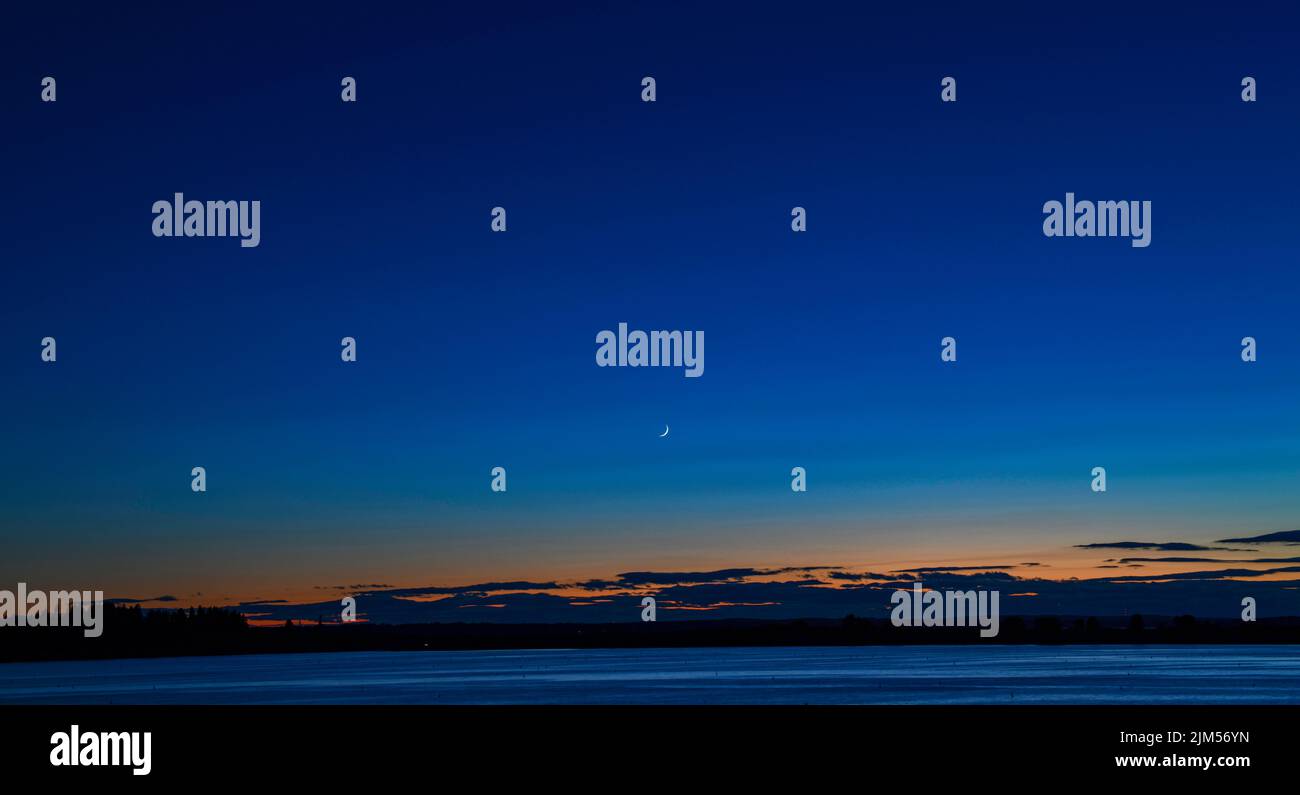 July 30 2022.  Barnes Island.  Post sunset view from Barnes Island.   Showing Whaleboat Island and waxing crescent moon.  Casco Bay, Maine Stock Photo