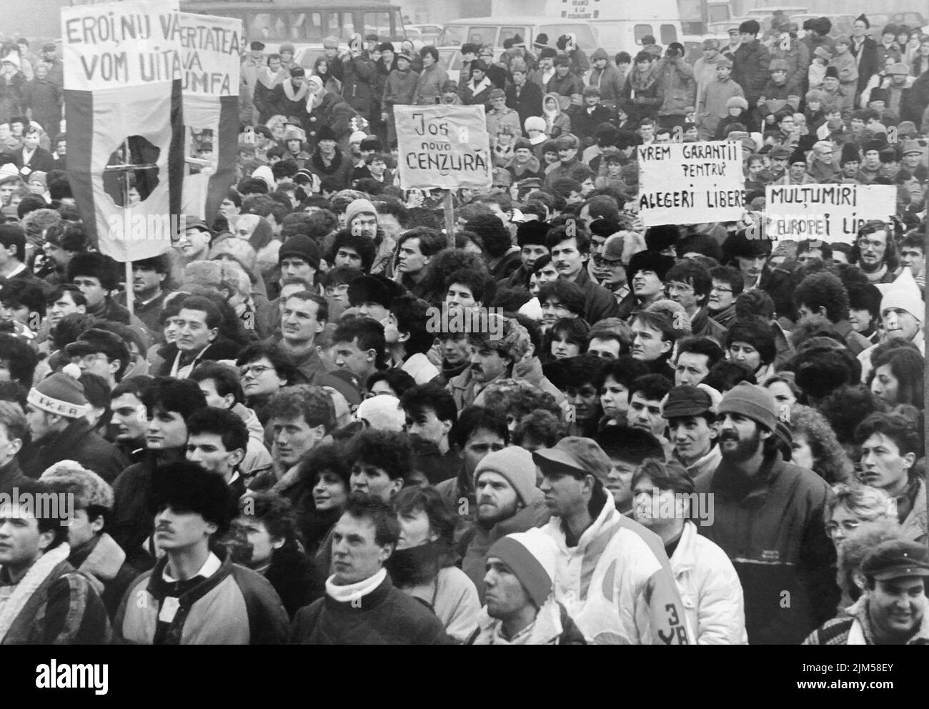 Bucharest, Romania, January 1990. Rally in the University Square following the Romanian Revolution of 1989. People would gather daily to protest the ex-communist officials that grabbed the power after the Revolution. The Romanian flag with the Socialist emblem cut off was an anti-communist symbol during the revolution. Banners saying 'Our heroes, we will never forget you', 'Freedom will triumph', 'Down with the new censorship', 'We want assurances for free elections', 'Thank you, Radio Free Europe'. Stock Photo