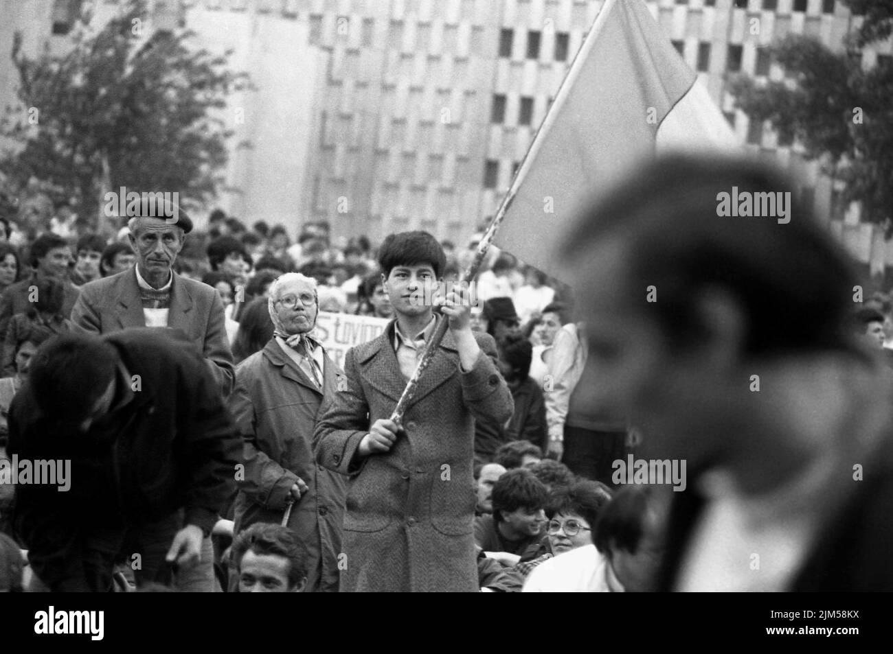 Bucharest, Romania, April 1990. 'Golaniada', a major anti-communism protest  in the University Square following the Romanian Revolution of 1989. People would gather daily to protest the ex-communists that took the power after the Revolution. The main demand was that no former party member would be allowed to run in the elections of May 20th. In this picture, a boy is waving the Romanian flag with the Socialist emblem cut off, an anti-communist symbol during the revolution. Stock Photo