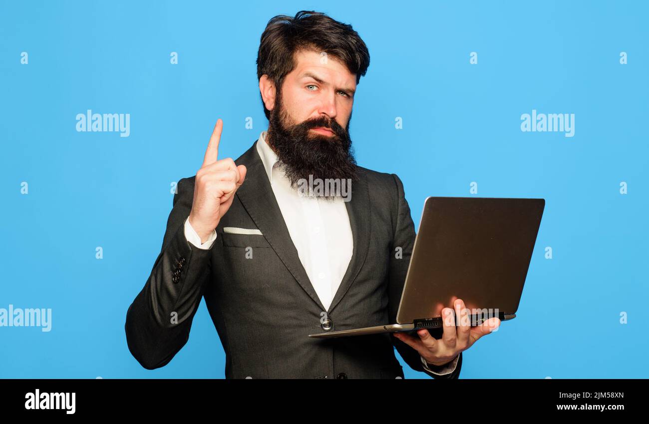 Bearded man with laptop computer pointing finger up. Businessman with notebook in office. Stock Photo