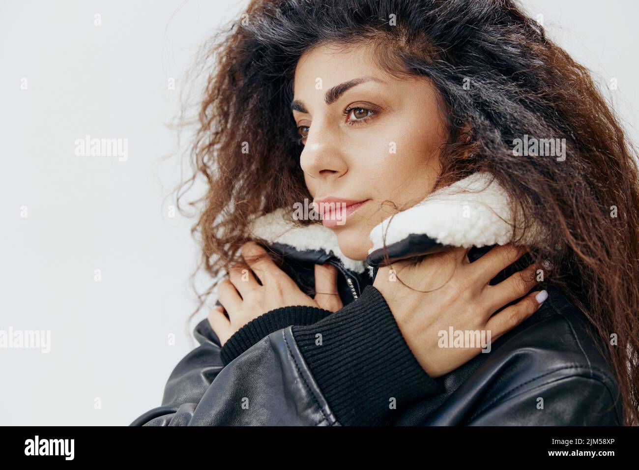 Close Up Of Thoughtful Curly Pretty Latin Lady Wrapping In Warm Leather Black Jacket With Fur Collar Looking Aside Posing Isolated At White Studio Stock Photo