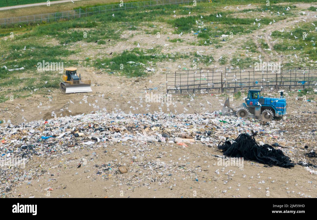 An aerial view above a garbage landfill while a trash compactor is working; seen during the day with many seagulls. Stock Photo