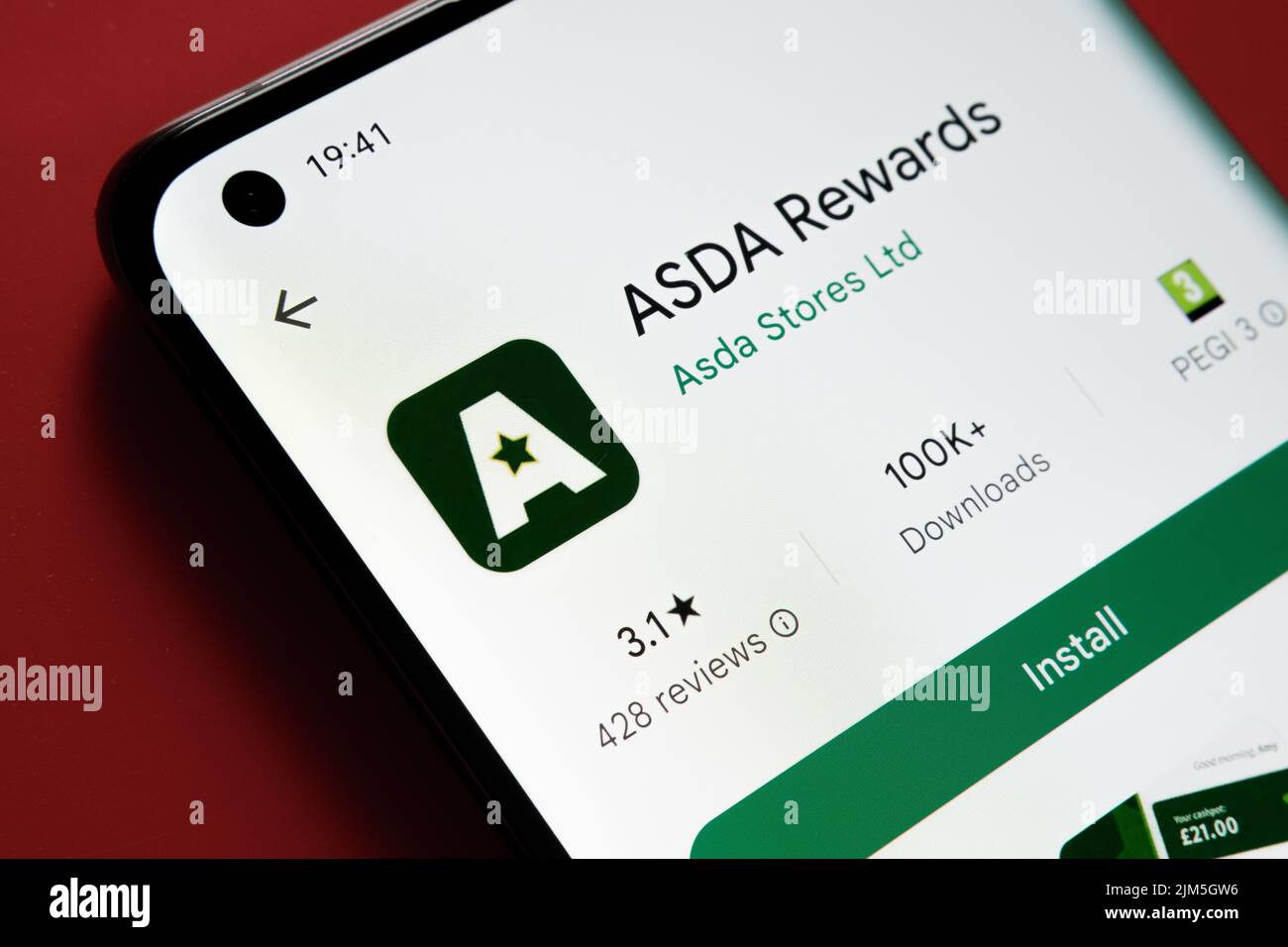 ASDA Rewards app seen in Google Play Store on the smartphone screen placed on red background. Close up photo with selective focus. Stafford, United Ki Stock Photo