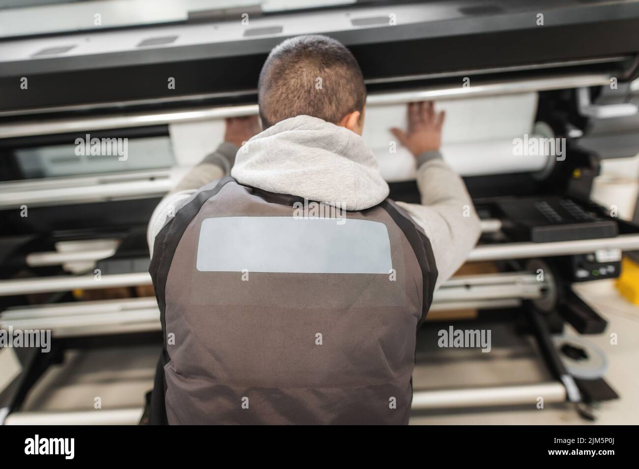 Technician worker operator changes the paper roll on large premium industrial printer and plotter machine in digital printshop office Stock Photo